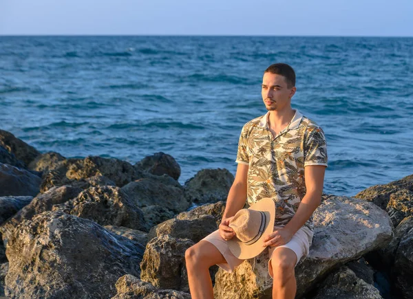 a young guy with a mustache sits on a stone on the shore of the Mediterranean Sea 3