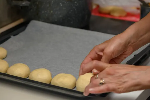 woman placing buns on a baking sheet