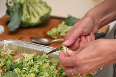 11 pişirmek için tavuk filetosuna brokoli kesen kadın.