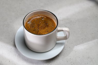 Mermer masa zemininde sütlü kahve fincanı ve çay tabağı güneş ışığının doğal geometrik gölgesi, günaydın markalaşma geçmişi.