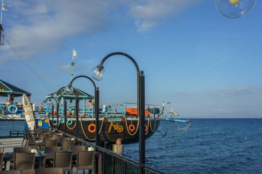 A lively pier stretches out into the clear blue waters, adorned with colorful buoys and lanterns, creating a perfect backdrop for relaxation and scenic views. clipart