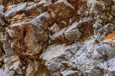 Doğal bir kaya oluşumunun detaylı bir görüntüsü, gri ve kahverengi minerallerin çeşitli katmanlarını gösterir, jeolojik süreçler tarafından şekillendirilen dokuları ve renkleri gösterir..