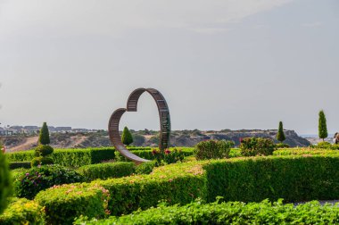 Canlı yeşilliklerin ortasında, kalp şeklinde güzel bir heykel gururla duruyor, ziyaretçileri berrak bir gökyüzü altında manzaralı kıyı manzarasına hayran olmaya davet ediyor..