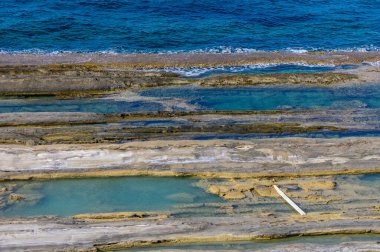 Low tide reveals stunning rocky formations along the coast, where clear blue waters reflect the sky, creating a serene natural beauty, inviting contemplation and exploration. clipart