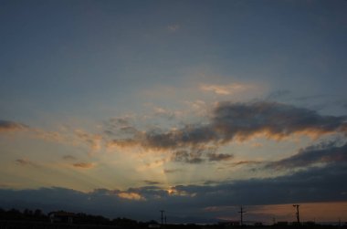 As day transitions to night, vibrant clouds dance in the sky, blending shades of orange and blue. Power lines silhouette against this peaceful backdrop, evoking tranquility. clipart