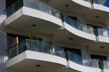 Contemporary balconies feature lush plants, capturing urban elegance against a vibrant blue sky backdrop. clipart