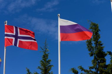 Two national flags flutter in the breeze, signaling friendship under a clear blue sky. clipart