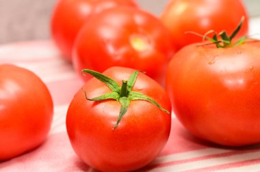 Juicy red tomatoes lie on a striped cloth, showcasing their vibrant color and freshness in a home cooking setting.