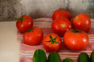 Freshly harvested tomatoes and cucumbers arranged beautifully on a soft, striped cloth in a warm kitchen. clipart