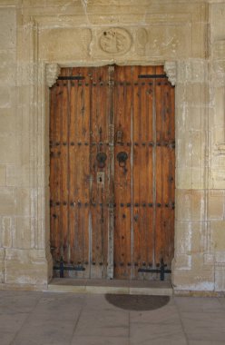 Weathered wooden doors with metal fixtures stand proudly in a sunlit, timeless architectural space. clipart