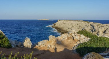 Golden sunlight illuminates rocky coastal cliffs, where crystal-clear waters gently crash against the shore. clipart