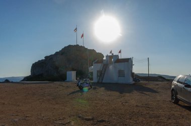 A cozy building stands near a rocky outcrop as the sun sets, casting warm light over flags fluttering gently. clipart