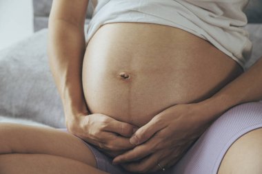 Kanepede oturan ve karnını tutan hamile bir kadın..