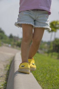 Dikey görüntü, küçük çocuk bacakları parkta kaldırımda yürüyor, yaz zamanı..