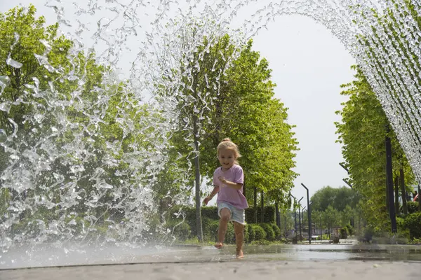 Little caucasian child running near fountain, barefoot. Happy smiling face. Summer time. Shot in motion.