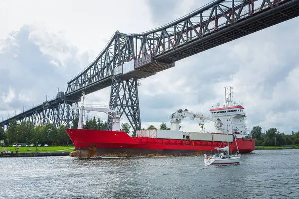 Almanya 'nın kuzeyinde Schleswig-Holstein eyâletinde, Rendsburg Kanalı' ndaki Rendsburg Yüksek Köprüsü 'nün altında bir kargo gemisi ve yelkenli geçidi.