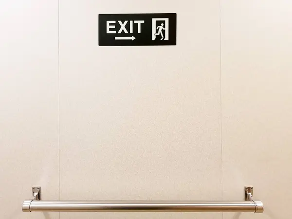 Exit sign on the wall placed above a metallic handle bar