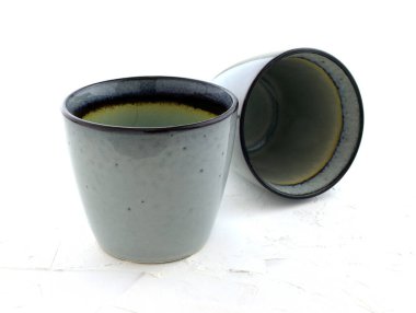 Beyaz arka planda sapı olmayan iki seramik bardak. Gri parlak gözlükler. Boş mavi bardak, el yapımı. Kafe ve ev için sofra takımı.