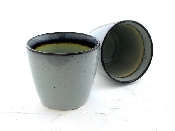 Beyaz arka planda sapı olmayan iki seramik bardak. Gri parlak gözlükler. Boş mavi bardak, el yapımı. Kafe ve ev için sofra takımı.