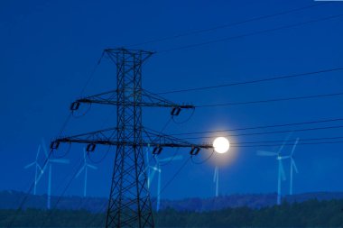 View of a high voltage line pylon, dark sky and moon in the background, symbolic image of power price crisis