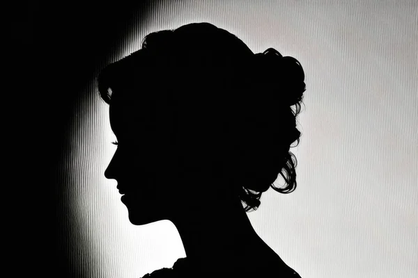 A woman in a black dress is silhouetted against a wall with a light shining on her backlighting a character portrait art photography