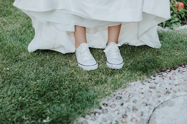feet of bride wearing white sneakers and wedding dress on green grass