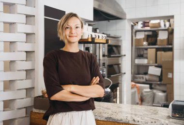 Portrait of smiling young woman entrepreneur standing at the counter of her bakery and coffee shop. Local small business owner indoors.