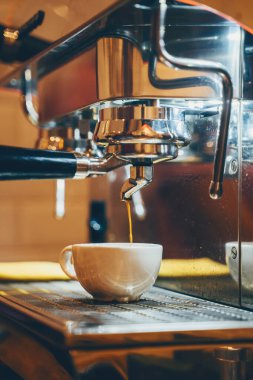 Professional coffee brewing in coffee shop. Close-up photo of espresso pouring from coffee machine. Barista make coffee cup in warm cozy atmosphere in small cafe.