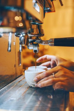 Professional coffee brewing in coffee shop. Close-up photo of espresso pouring from coffee machine. Barista make coffee cup in warm cozy atmosphere in small cafe.