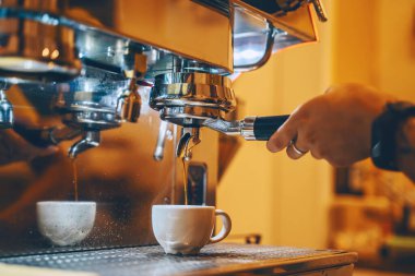 Professional coffee brewing in coffee shop. Close-up photo of espresso pouring from coffee machine. Barista make coffee cup in warm cozy atmosphere in small cafe.