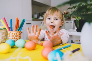 Smiling little girl with colorful eggs preparing for Easter Holiday. Kids painting easter eggs. Creative background for preschool and kindergarten. Family traditions and symbols of celebration.