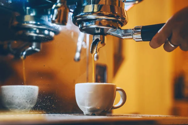 Professional coffee brewing in coffee shop. Close-up photo of espresso pouring from coffee machine. Barista make coffee cup in warm cozy atmosphere in small cafe.