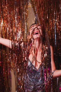 Mutlu kadın yeni yılı kutluyor. Gümüş parıltılı elbiseli güzel bir kadın yılbaşı partisinde eğleniyor. Tatil kutlaması. Genç kız mutluluk ve şaşkınlık duygularını ifade eder..