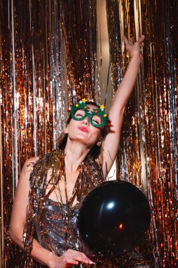 Mutlu kadın yeni yılı kutluyor. Gümüş parıltılı elbiseli güzel bir kadın yılbaşı partisinde eğleniyor. Tatil kutlaması. Genç kız mutluluk ve şaşkınlık duygularını ifade eder..