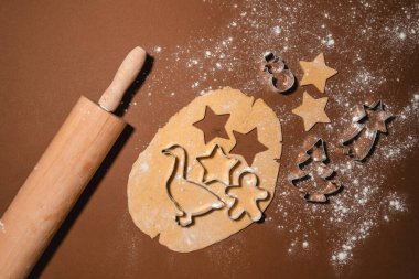 Çiğ Noel Kurabiyeleri. Kurabiye kesiciyle zencefilli ekmek yapma süreci. Zencefilli ekmek hamuru, kurabiye şekilleri ve masaya saçılmış un ile merdane tokası. Düz, minimalist