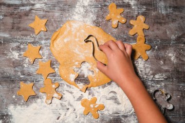 Çocuklu bir aile masaya un serpiştirilmiş Noel kurabiyeleri hazırlıyor. Çocuk elleri hamurdan kurabiye keskisi ile zencefilli ekmek yapıyor. Düz, minimalist