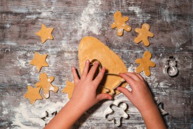 Çocuklu bir aile masaya un serpiştirilmiş Noel kurabiyeleri hazırlıyor. Çocuk elleri hamurdan kurabiye keskisi ile zencefilli ekmek yapıyor. Düz, minimalist