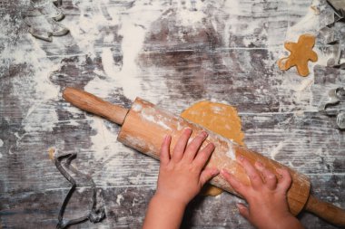 Çocuklu bir aile masaya un serpiştirilmiş Noel kurabiyeleri hazırlıyor. Çocuk elleri hamurdan kurabiye keskisi ile zencefilli ekmek yapıyor. Düz, minimalist