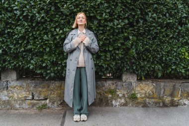 Yeşil yaprakların arka planında gözleri kapalı rahatlamış bir kadın portresi. Ofis dışı kavram, İş-Hayat-Dengesi, Mola. Zen ve insanları dengelemek. Ruh sağlığı yoluyla istikrar.