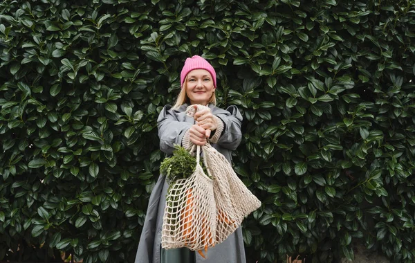 Mujer Sonriente Con Zanahorias Orgánicas Frescas Bolsa Malla Contra Pared Imágenes de stock libres de derechos