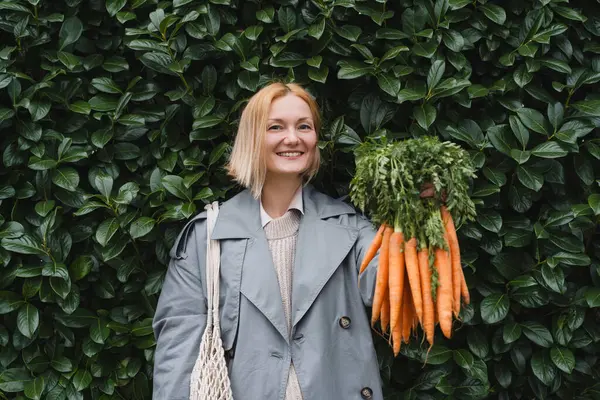 Mujer Sonriente Con Zanahorias Orgánicas Frescas Contra Pared Hojas Verdes Imagen de stock