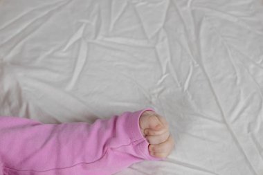 Yatakta yatan 4 aylık küçük bir kız çocuğu. Bebekler pembe elbiseler içinde beyaz arka plan.