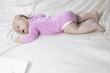 Sevimli ve güzel 4 aylık bir kız bebek yatakta yatıyor. Beyaz arka planda pembe tulumlu bir bebek..