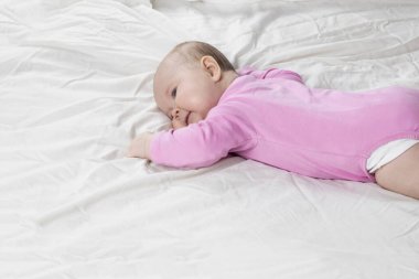 Sevimli ve güzel 4 aylık bir kız bebek yatakta yatıyor. Beyaz arka planda pembe tulumlu bir bebek..