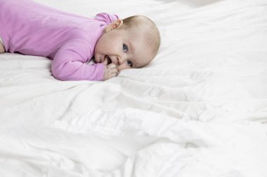 Sevimli ve güzel 4 aylık bir kız bebek yatakta uzanıyor ve kameraya bak. Beyaz arka planda pembe tulumlu bir bebek..