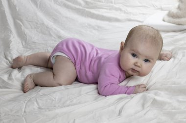 Sevimli ve güzel 4 aylık bir kız bebek yatakta yatıyor. Beyaz arka planda pembe tulumlu bir bebek..