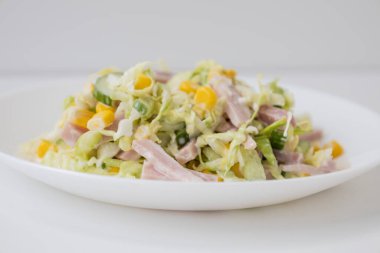 Beyaz tabakta lahana, salatalık, mısır, jambon ve mayonez ile lezzetli ve sağlıklı bir salata..