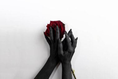 The black hands with long nails hold a rose and make it dry. Concept photo with woman hands painted in black paint with hold a red flower. Demon power in hands make rose die clipart