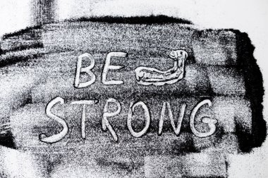 Siyah parıltılarda BE STRONG ve beyaz arka planda kaslı kol kelimeleri çiziyor. Parıltıdan soyut minimalist kompozisyon