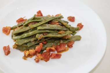 Domates ve soğanlı kızarmış yeşil fasulye. Yemekte fasulyeli lezzetli yemek ya da beyaz tabakta öğle yemeği.
